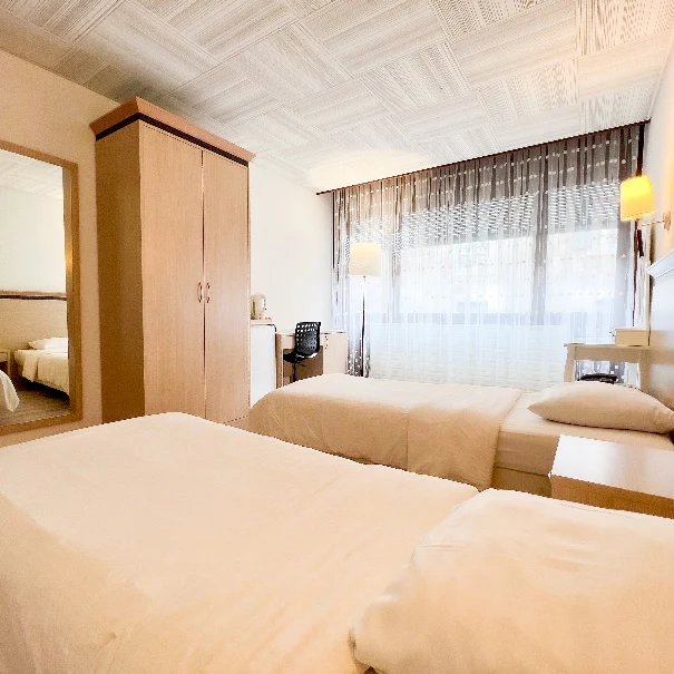 Twin-bed student room with a wardrobe, desk and large window